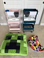Photo displaying two 3-tiered rolling storage carts (pink and dark green) alongside a Minecraft pillow and a colorful lap desk.