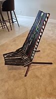 Side view of chair made with vertically aligned hockey sticks as seat and backrest, supported by metal frame base.