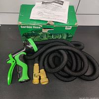 Complete set: green-and-black water sprayer, black expandable hose coiled, brass connectors, and original green box with instructions on top.