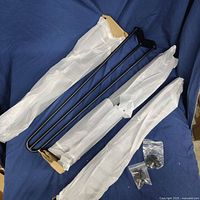 Four matte black steel hairpin table legs wrapped in protective fabric with mounting hardware on a blue background.