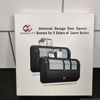 Front of box showing two black remotes with three silver buttons for universal garage door opener remote control by Creacity.