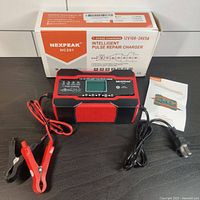 Image showing the complete charger unit with attached cables, clamps, power cord, instruction manual, and product box.