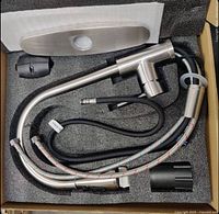 Top-down view of the new kitchen faucet in packaging showing faucet body, hoses, deck plate, and other installation parts.