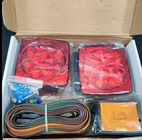 Photo of the unboxed contents showing two red square LED trailer lights, amber side marker, wiring harness, and mounting hardware inside the box.