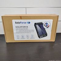 Photo of the packaging box showing SoloForce branding, product image, and key features including 20000mAh battery, wireless charging, solar panel, and LED lights.