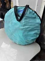 Light blue circular carrying bag with zipper and black handles, containing the foldable wind sail.
