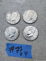 Four USA half dollar coins laid out on a grey surface with a blue tape labeled '# 71 x 4'. The coins are dated 1972, 1974, 1976, and 2001.