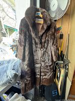 Front view of a brown mink fur coat hanging, showing button closure and fur texture under natural light.