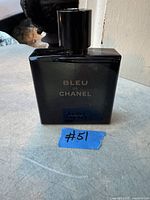 Dark blue glass bottle of Bleu de Chanel Parfum with black cap placed on a grey surface. Label text visible on front of bottle.