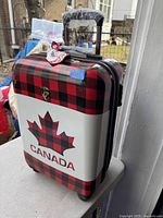 Exterior front view of the carry-on suitcase showing red and black checkered pattern with large maple leaf and Canada text.