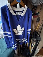 Blue CCM Toronto Maple Leafs sweater hanging on a hanger, showing front with logo and white stripes on sleeves and waist.