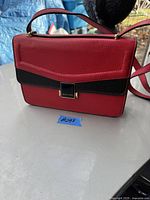 Image showing a red and black rectangular Celine Dion purse with gold-tone hardware, single top handle, and shoulder strap on a table.