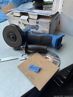 Mastercraft cordless angle grinder 4 1/2 inch with attached grinding disc, wrench tool, additional grinding disc in cardboard sleeve, and original box.