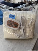 Electric blanket folded and packed in clear plastic bag, showing controller, power cord, and folded blanket texture and color.