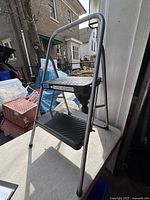 Front angle of two-step folding ladder showing side rail and steps on a concrete surface near a doorway.