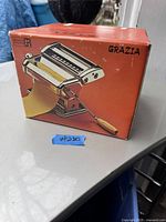 Photo of the original orange box showing the Grazia Modello 150 pasta maker with wooden handle and pasta dough being rolled through the machine.