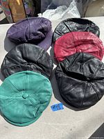 Top view showing all six leather ladies hats/caps in purple, black, red, and green shades.