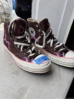 Front and side view of the brown canvas Converse high tops with white laces and red-lined rubber midsoles showing flame design.