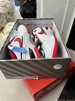 Top-down angle showing both shoes side by side inside original shoebox, displaying white base color with red Nike swoosh and outsole accents.