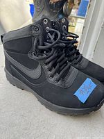 Side view of black Nike winter boots showing lace-up design, high ankle support, and Nike swoosh logo.