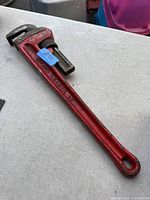 Full view of the red 18-inch pipe wrench laid on a gray surface, showing the entire length and handle including embossed 'Record Leader 18' marking.