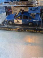 Front angled view of the blue RCMP emergency model car in clear display case showing detailed police logo, light bar, and 'Emergency 9-1-1' text on side door.