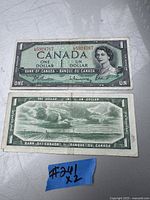 Two Canadian one dollar bills lying flat, front and back visible, showing portrait of Queen Elizabeth II and a scenic back with boats and canoe.