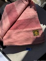 Folded pink wool blanket showing gradient shades and sewn brand label.