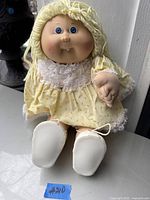 Front view of the vintage Cabbage Patch Kids doll wearing an original yellow dress and white shoes.