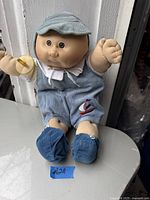 Front view of vintage Cabbage Patch doll seated, wearing light blue corduroy romper with sailboat emblem and matching shoes.