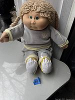 Full view of vintage Cabbage Patch Kids doll in original grey and yellow outfit with braided yarn hair and green eyes.