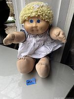 Full front view of vintage Cabbage Patch doll sitting on a white surface, showing face, hair, and full outfit.