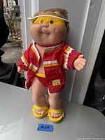 Front view of the doll showing original red and yellow jacket, yellow swimsuit bottom, yellow sandals, and white visor.