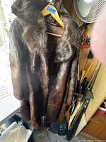 Front view of the vintage ladies fur coat hanging showing dark brown fur and high collar against a wooden wall and tools.