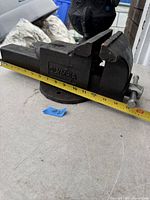 Side angled view showing the 'OLYMPIA' embossed on the body of the bench vice with measuring tape indicating size.