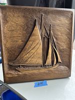 Wooden carved relief featuring detailed view of the Bluenose II sailing ship, colored in warm brown tones and showing full sails and hull.
