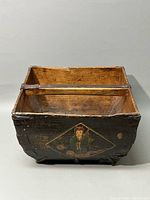 Front view of square wooden bucket showing painted figure and wooden handle.