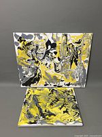 Two abstract oil paintings on canvas with yellow, black, white, and gray swirling patterns. Larger canvas approximately 20x16.5 inches, smaller canvas smaller in size, both with textured, marbled effect brushwork.
