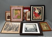Collection of eight framed art lithographs arranged on a grey surface showing various styles and subjects