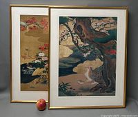 Two framed Asian lithographs featuring birds and nature, with an apple for scale.