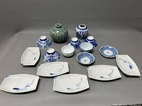 Overview photo showing all items including six blue and white bowls, five rectangular plates with fish designs, and two decorative vases arranged on a grey background.