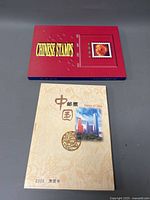 Two hardcover Chinese stamp collection books: one red from 1997 labeled 'Chinese Stamps' with a flower stamp image, and one beige from 2000 labeled 'Stamps of China' featuring a golden coin and cityscape image.