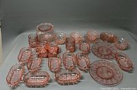 Full view of all pink Depression glass items arranged on white surface including vase, cups, saucers, plates, and serving trays.