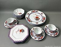 Full set showing 3 bowls stacked, 4 dinner plates stacked, 3 cups with saucers arranged front, and 4 salad plates stacked left side.