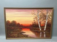 Full view of the framed sunset landscape oil painting showing a river, trees, and a vibrant sky.