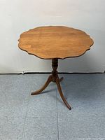 Full view of wooden end table showing scalloped round top and pedestal base with three legs.