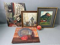 Four oil paintings grouped on a table, including two framed paintings and two unframed, showing still life and landscapes.