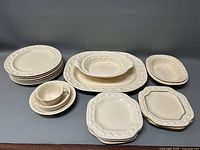 Front view showing the set of white off-white ceramic dinnerware including plates, bowls, platter, and vegetable dishes with embossed decorative borders.