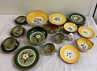 Full view of the 29-piece Stangl Pottery set arranged on a white tablecloth showing bowls, plates, cups, saucers, and gravy boat with hand-painted floral and fruit patterns in green, yellow, and brown.