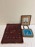 Asian handbag with crane embroidery, hand-woven red patterned mat, and framed embroidery art against a white background
